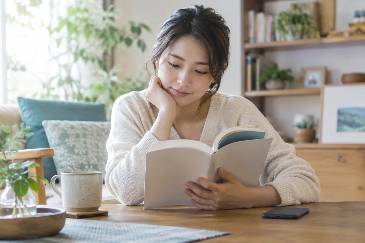スマートフォンを伏せ、一冊の本に集中する成人